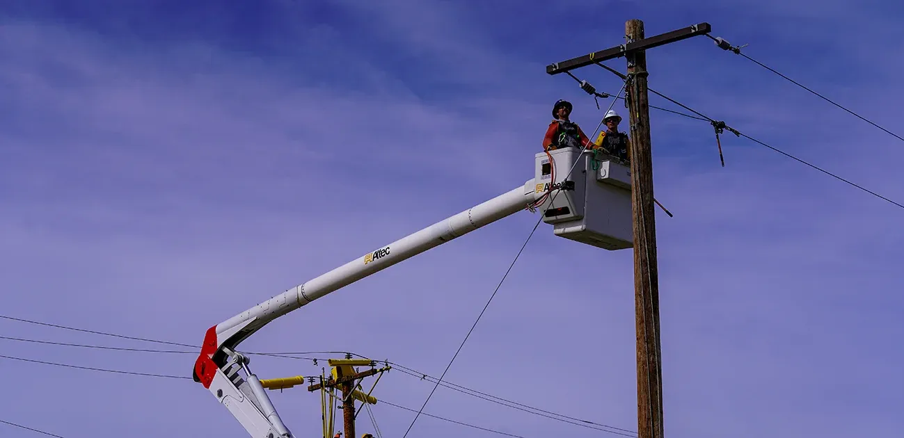 Two linemen in a bucket truck inspecting a distribution pole.